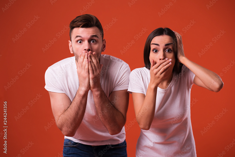 Shocked young couple in white t-shirts are closed mouth with help of hands Shocked young couple in white t-shirts are closed mouth with help of hands