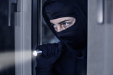 Einbrecher mit Taschenlampe steigt durchs Fenster ein 