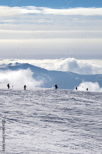 Silhouettes of skiers and snowboarders on snowy ski slope and mountains