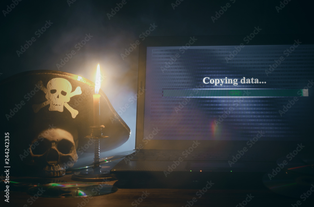 Fototapeta premium Koncepcja nielegalnego kopiowania danych. Cyberprzestępczość. Piractwo komputerowe tło. Piracki kapelusz, ludzka czaszka, laptop i płyta kompaktowa na stole.