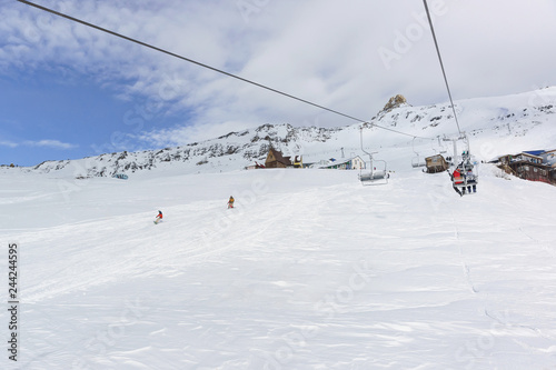 A two-seat cable car and a ski track with snowboarders in the ski resort of Dombay in the middle of the winter season