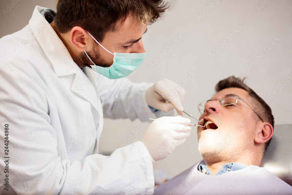 Serious young male dentist examining mature male patient in dental clinic