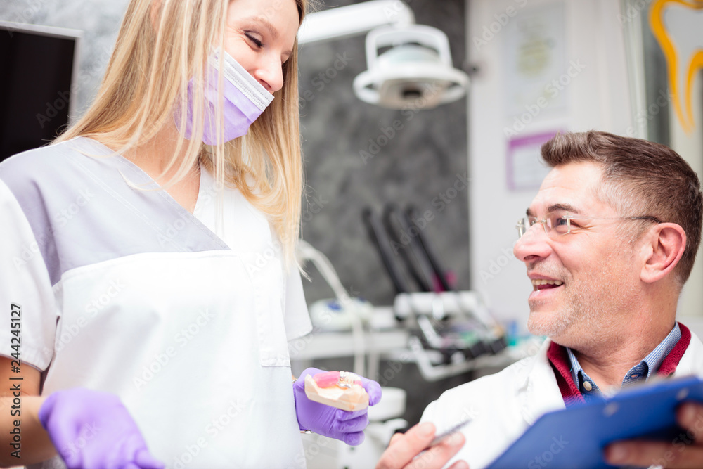 Mature male dentist discussing and talking with young female technician, working together in a dental clinic