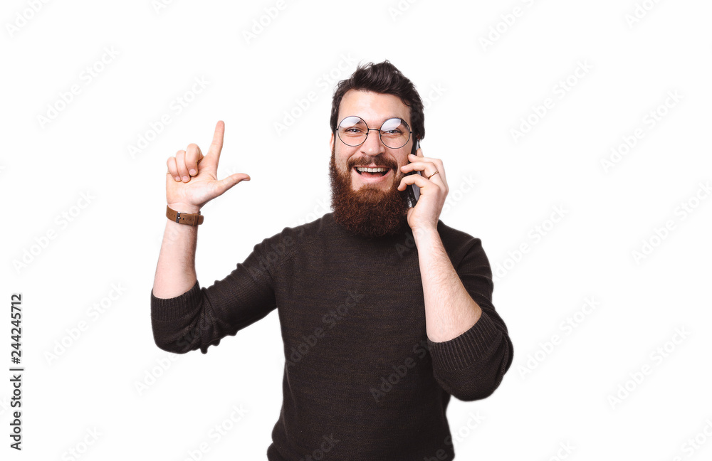 Handsome smart bearded boy ipoints up at copy space while talking on phone Handsome smart bearded boy ipoints up at copy space while talking on phone