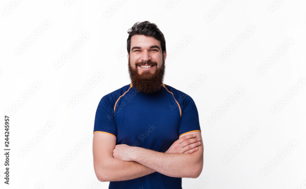 Attractive bearded sportsman in sport tshirt with crossed hands smiles and looks at the camera