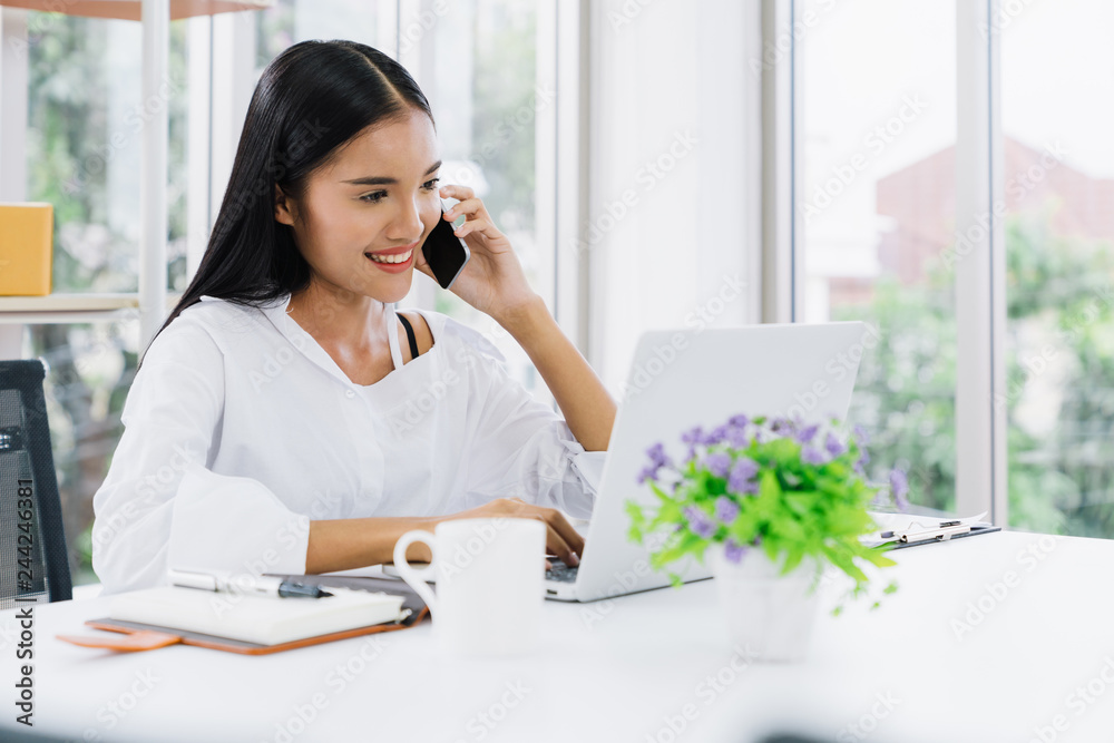 Young asian casual businesswoman using mobile phone and laptop to communicate with customer for order purchasing abd delivering information in modern home office, online shopping business concept Young asian casual businesswoman using mobile phone and laptop to communicate with customer for order purchasing abd delivering information in modern home office, online shopping business concept