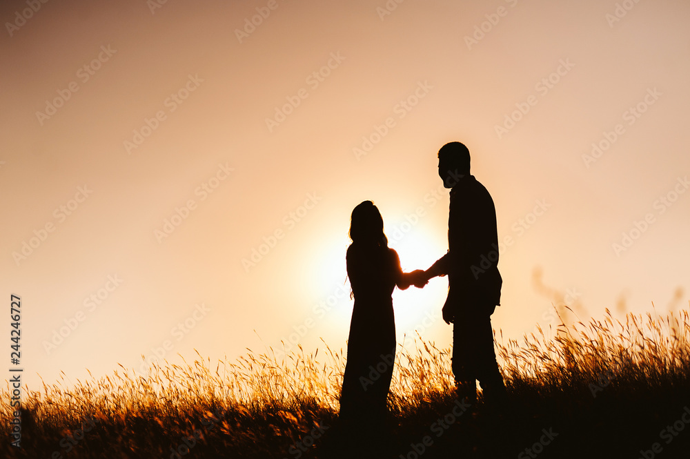 Couple silhouette in meadow on sunset, or sunrise