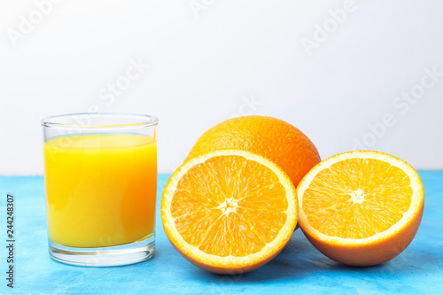 Glass of the fresh orange juice and ripe citrus fruits on a blue table and white background
