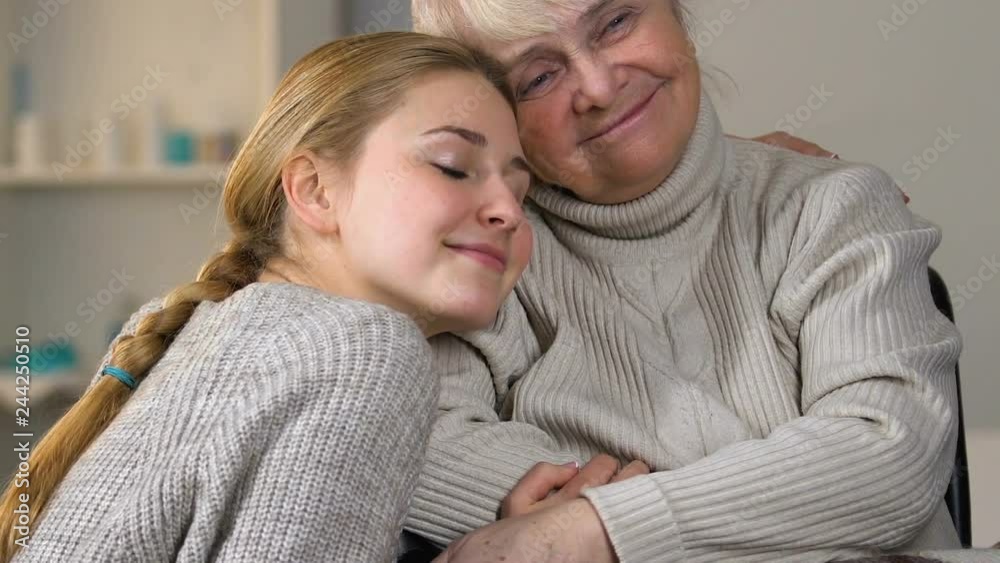 Attentive young lady covering disabled granny in wheelchair with plaid, hugging Attentive young lady covering disabled granny in wheelchair with plaid, hugging