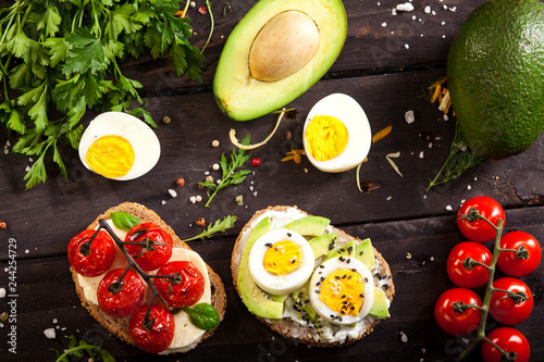 Bruschetta with avocado, cheese, egg, sesame, smoked cheese, cherry tomatoes, basil on a wooden table.