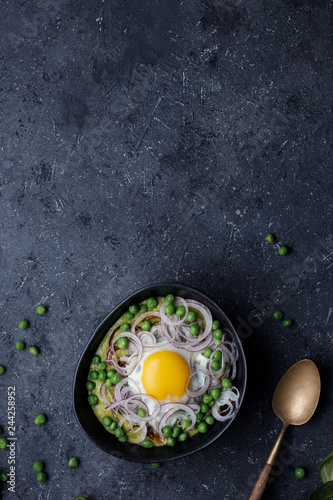Green pea soup with fried egg and red onion on dark background, top view.