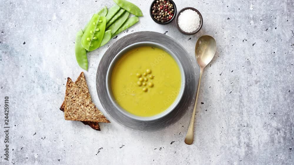 Green pea cream soup in grey bowl placed with spices, fresh peas, full grain bread on stone background. Top view with copy space. Green pea cream soup in grey bowl placed with spices, fresh peas, full grain bread on stone background. Top view with copy space.
