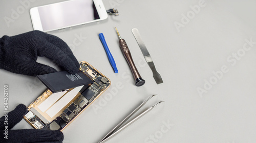 Technician or engineer disassembling components broken smartphone and take off battery for repair or replace new smartphone battery on desk with copy space