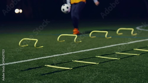 Soccer player with a ball, agility training equipment in front at night. 4k slow motion