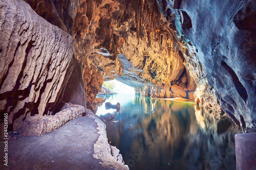 Sun light enter the mouth of the cave and the arch reflects in the turquoise water of the underground river