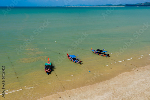 Aerial view of brightly colored traditional wooden Longtail boats moored off a sandy, tropical beach