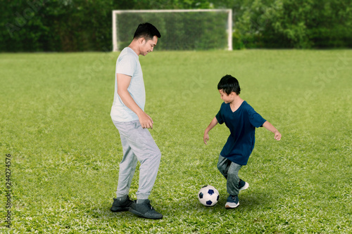 Child and father playing football in the field © Creativa Images