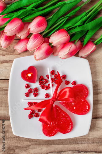 Fototapeta Naklejka Na Ścianę i Meble -  Lollipops in the form of a heart on a plate with candles and tulips flowers. Festive background to the Valentine's day.