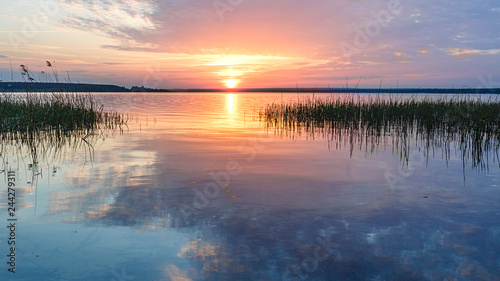 The rays of the dawn sun on the lake. Reflection of sunset clouds in the river. Rural landscape.