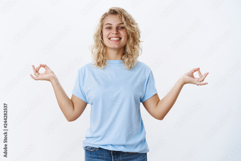 Fototapeta premium Keep calm and carry on. Portrait of optimistic relieved and stress-free good-looking female with blond hair smiling pleased and relaxed, standing in meditating pose in nirvana, showing orbs