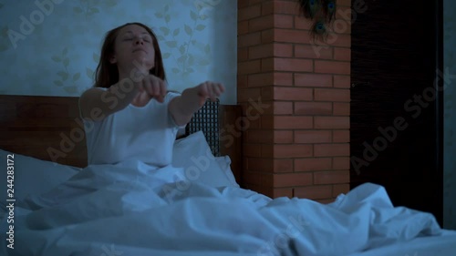 lunatic sits on the bed with his eyes closed and holds his arms outstretched in front of him.
