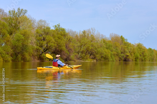 Spring kayaking. Concept for adventure, travel, action, lifestyle. Rear view of kayaker man paddle yellow kayak on Danube river.