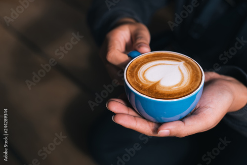 Young woman holding hot cup of coffee latte in coffee shop or home,copy space.