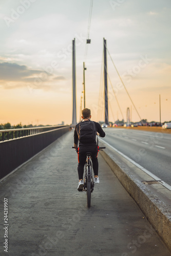 Man Riding Bicycle Across Bridge at Sunset