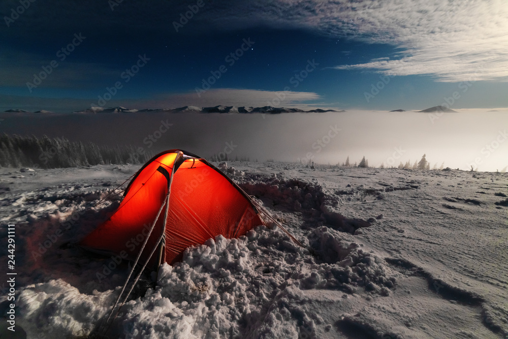 Clear, moonlit night, on a snow-covered mountain ridge with a highlighted red tent.