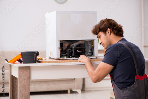 Young handsome contractor repairing fridge 