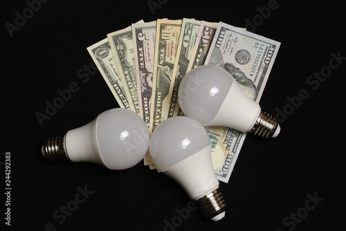 Energy saving light bulb on black background with money.