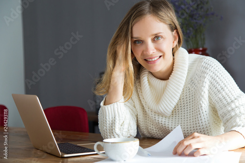 Smiling pretty woman analyzing report data in cafe. Positive young lady in white sweater working with business data. Paperwork concept