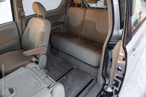 The interior of the car in the back of a minivan with a wide open automatic door and a view of the front and rear seats in beige color © Aleksandr Kondratov
