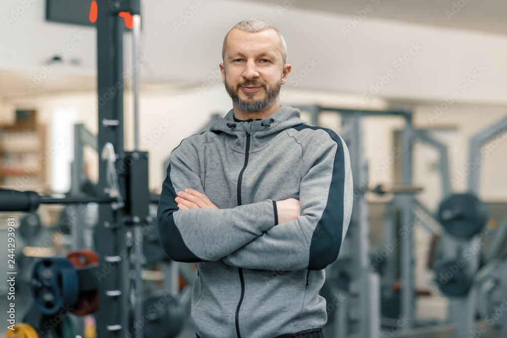 Portrait of sporty man with folded hands in gym, handsome bearded trainer looking at the camera Portrait of sporty man with folded hands in gym, handsome bearded trainer looking at the camera