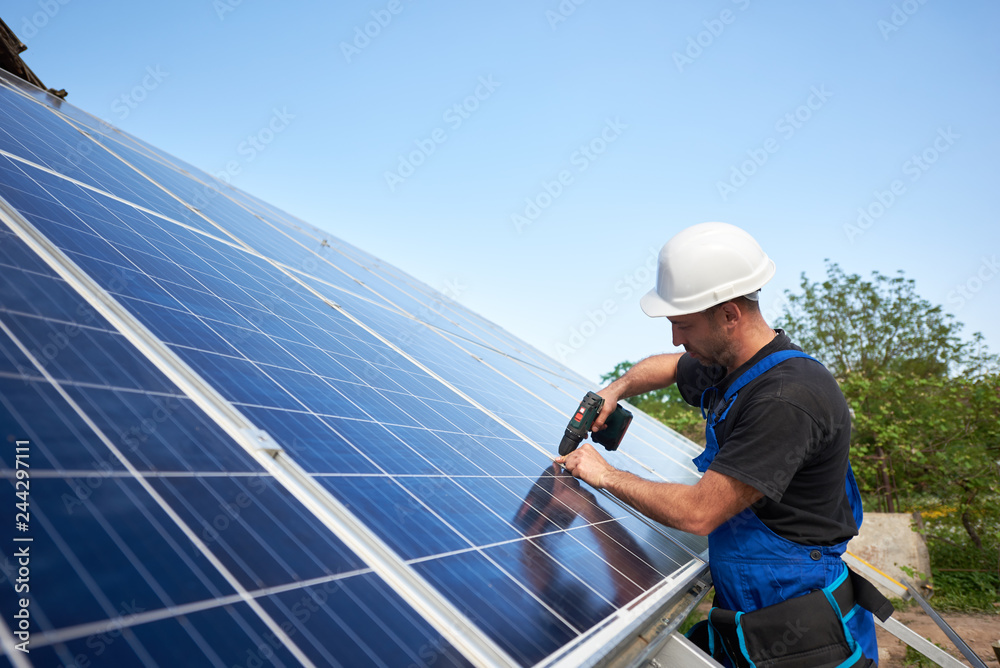 Technician connecting solar panel to metal platform using electrical screwdriver on blue sky copy space background. Stand-alone solar system installation, efficiency and professionalism concept. Technician connecting solar panel to metal platform using electrical screwdriver on blue sky copy space background. Stand-alone solar system installation, efficiency and professionalism concept.