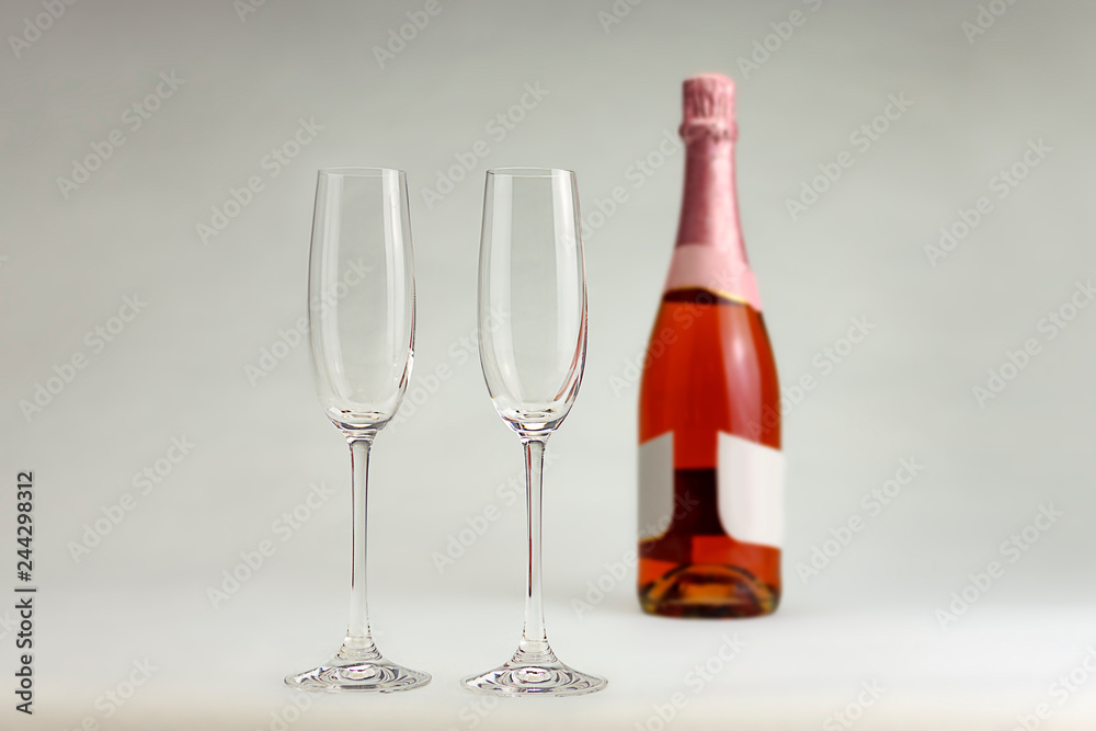 Two crystal copes with a bottle of champagne rose in a white background. Two crystal copes with a bottle of champagne rose in a white background.