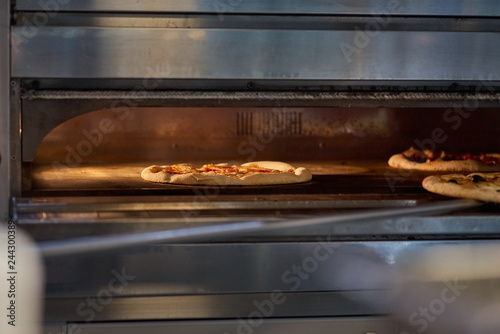 Cook putting Italian pizza to bake in oven. Preparation of pizza. selective focus, copy space. © izikmd