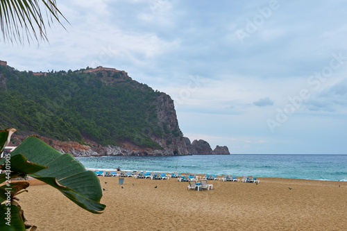 Fototapeta Naklejka Na Ścianę i Meble -  Empty sandy Cleopatra beach on a rainy day with fisherman, Alanya, Turkey.