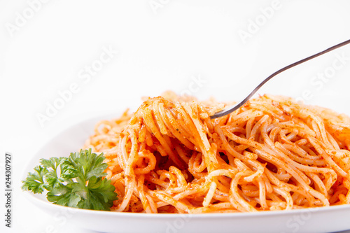 Spaghetti with pesto rosso decorated with parsley eaten with a fork on a white background