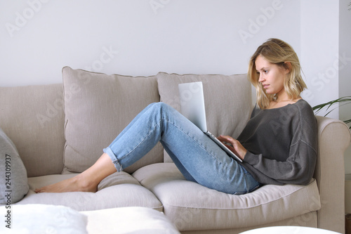 Junge Frau sitzt auf einem Sofa und arbeitet mit einem Laptop