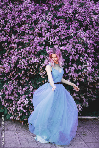 The red-haired girl dances and is spinning in a luxurious, dignified, lilac, purple dress. Fabric beautifully flies in motion. The background is a fantastic garden.
