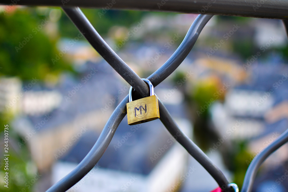 Close up of a gold padlock with M and V letters, with a blurred colorful background Close up of a gold padlock with M and V letters, with a blurred colorful background