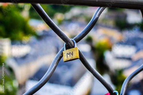 Close up of a gold padlock with M and V letters, with a blurred colorful background