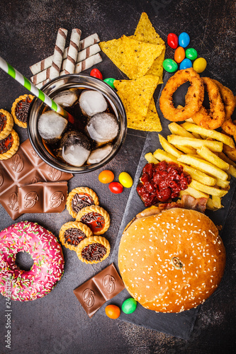 Junk food concept. Unhealthy food background. Fast food and sugar. Burger, sweets, chips, chocolate, donuts, soda, top view.