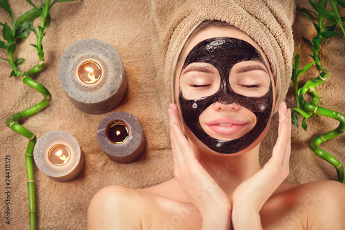 Beautiful woman with black purifying black mask on her face. Beauty model girl with black facial peel-off mask lying in spa salon. Skincare, cleansing photo
