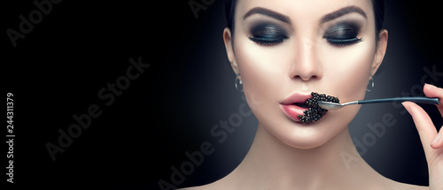 Beautiful fashion model woman eating black caviar. Beauty girl with caviar on her lips isolated on black background