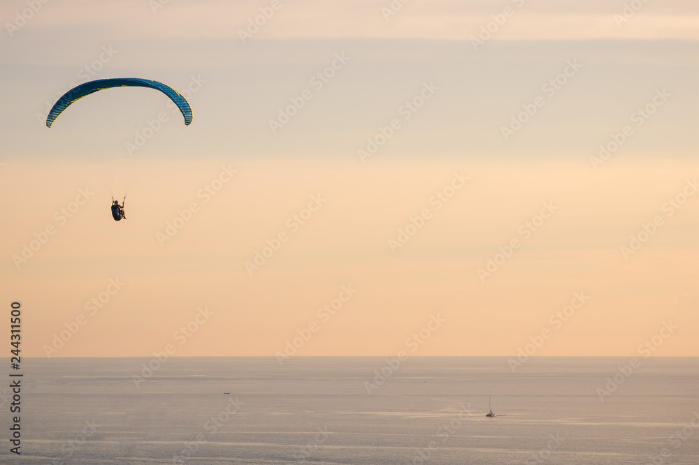 Skydiving of parachutist flying at sunset sky and sea background