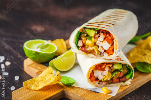 Foto Burritos wraps with chicken, beans, corn, tomatoes and avocado on wooden board, dark background