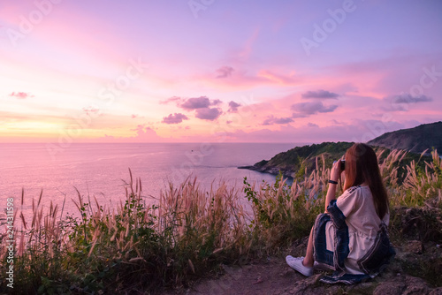 young woman sit on stone and use mobile phone takes a photo with beautiful amazing sea sunset of orange red colors