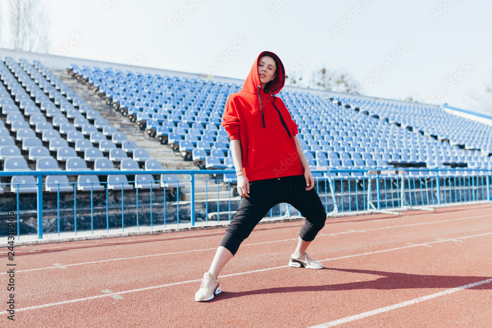Fototapeta premium Beautiful girl in sportswear standing on the running track and preparing to run. Morning warm-up before exercise.